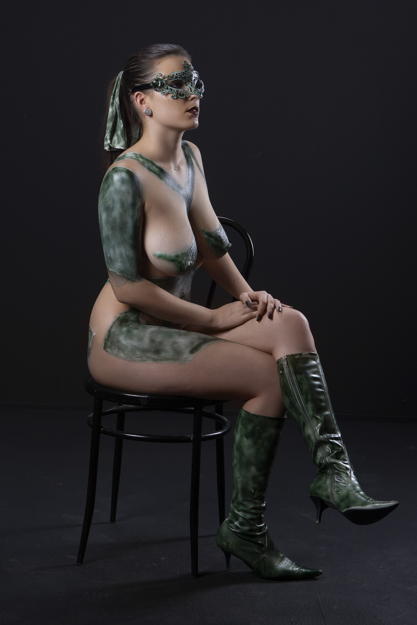 Eine Frau sitzt nackt auf einem Stuhl, ihr Körper kunstvoll mit leuchtendem Bodypainting bedeckt
